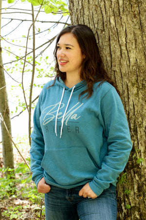 Model in blue Bella Rider sweatshirt leaning on tree